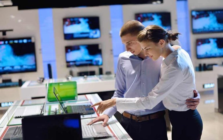 Junges Paar lässt sich im Elektronikfachmarkt beraten: Professionelles Duftmarketing im Technik-Einzelhandel beeinflusst das Verbraucherverhalten und die gemeinsame Kaufentscheidung positiv.